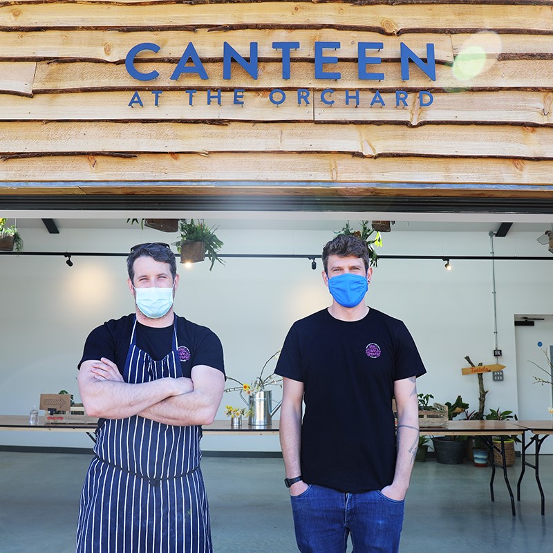 Ben and Paul stand in the doorway at Canteen at the Orchard with the sign above them