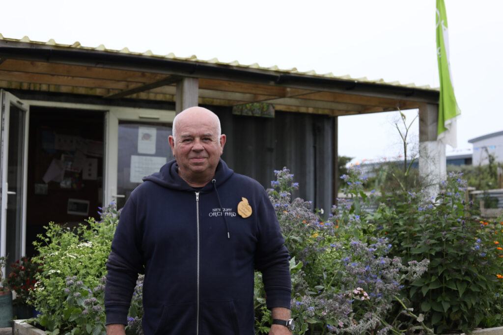 John wearing a "Newquay Orchard" hoodie standing in front of a wooden building, surrounded by flowering borage and other blooms.